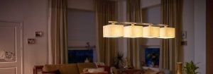 Модерна висяща LED лампа с множество текстилни нюанси осветява уютна всекидневна, демонстрирайки енергийно ефективни и стилни решения за домашно осветление за атмосфера на вечерен комфорт.